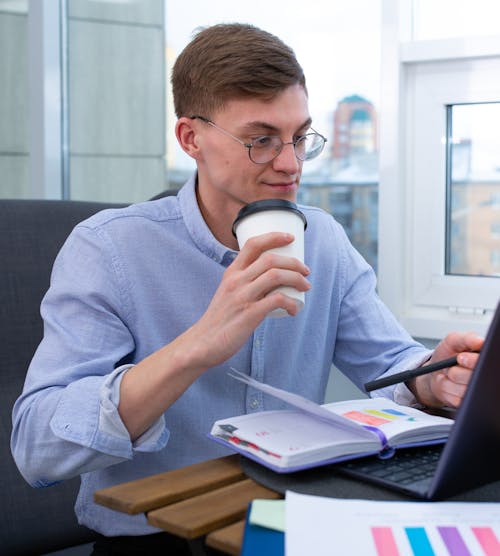 A Man Wearing Eyeglass Holding a Coffee Cup While Working
