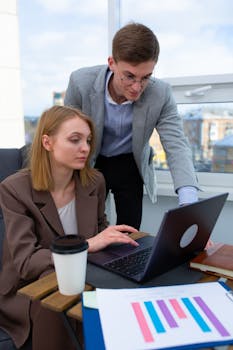 Two colleagues collaborating on a project with laptop and documents in a modern office.