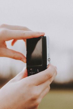 Close-up of hands holding a compact digital camera outdoors, with selective focus on the camera.