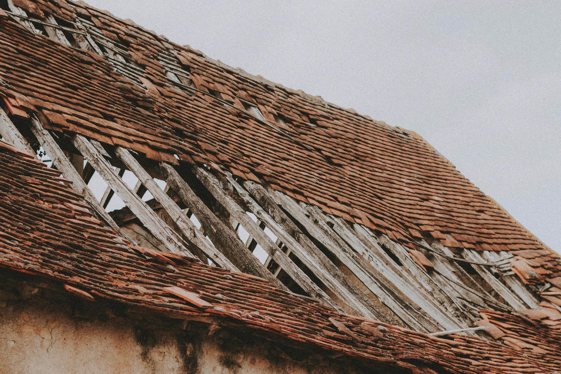 A close-up of an old, dilapidated roof with missing shingles and wooden beams.