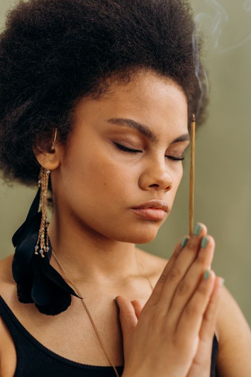 Free Young African American woman meditating with incense stick for a calming ritual. Stock Photo