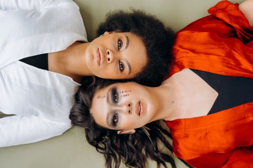 Free Two women in white and red outfits lying down, highlighting diversity and togetherness. Stock Photo