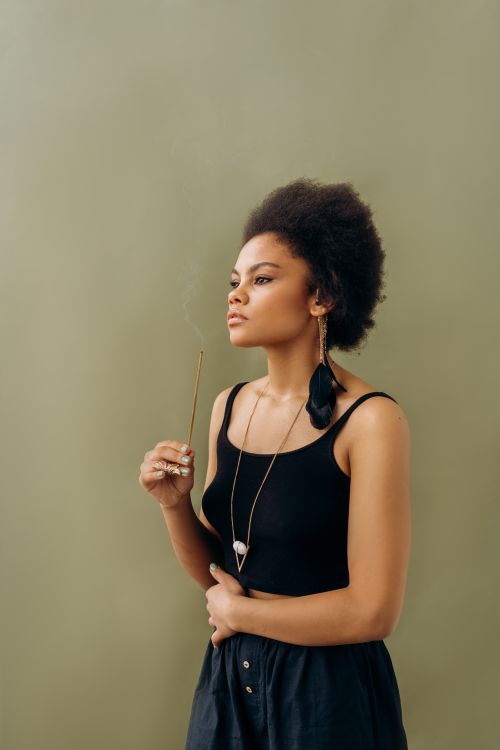 Free Young woman with afro hair holding incense, embodying calmness and relaxation. Stock Photo