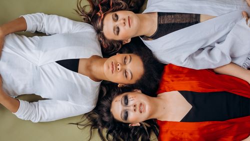 Free A peaceful scene of three women lying down with eyes closed, wearing colorful clothing. Stock Photo
