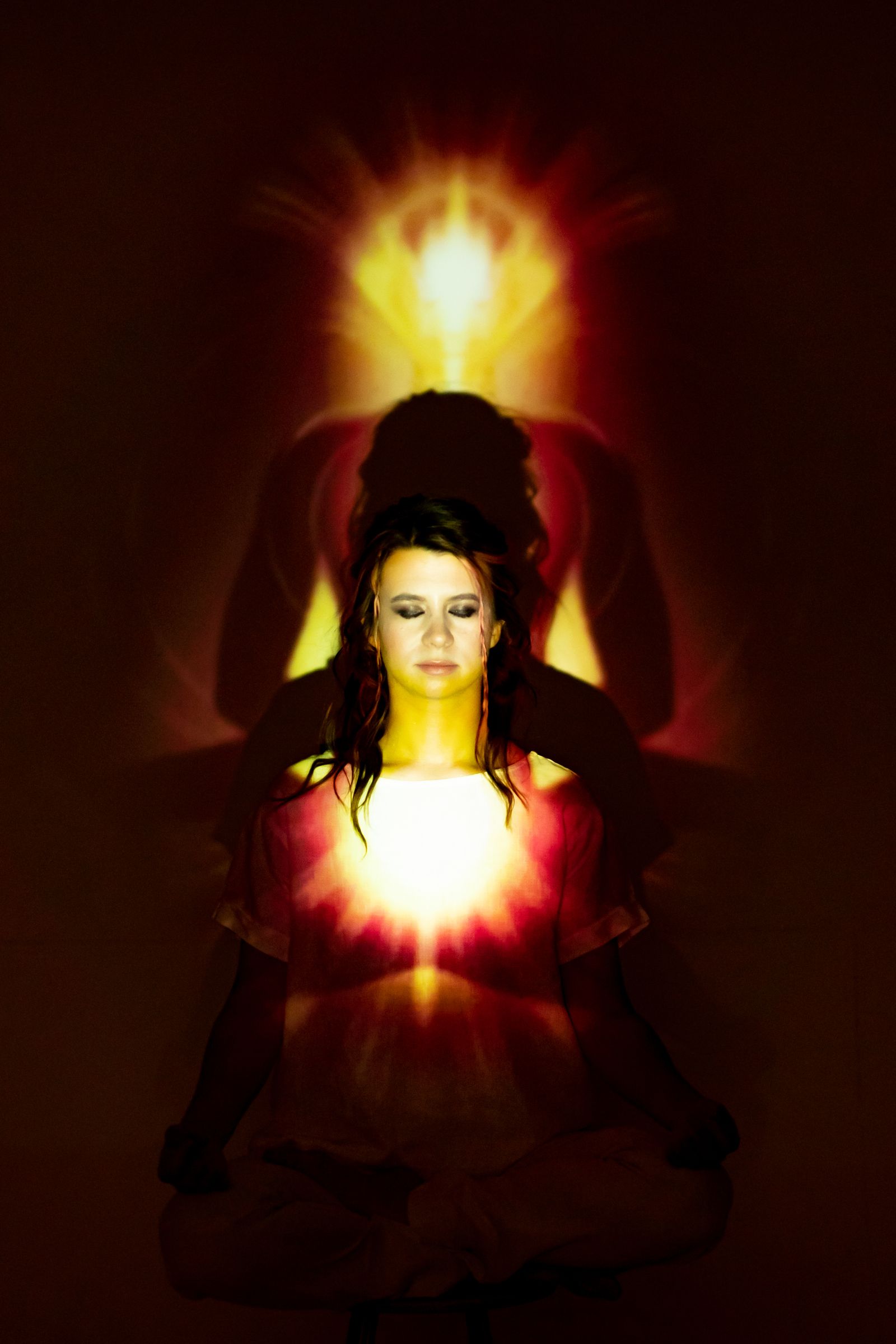 Woman seated in lotus meditation position surrounded by vibrant coloured aura light