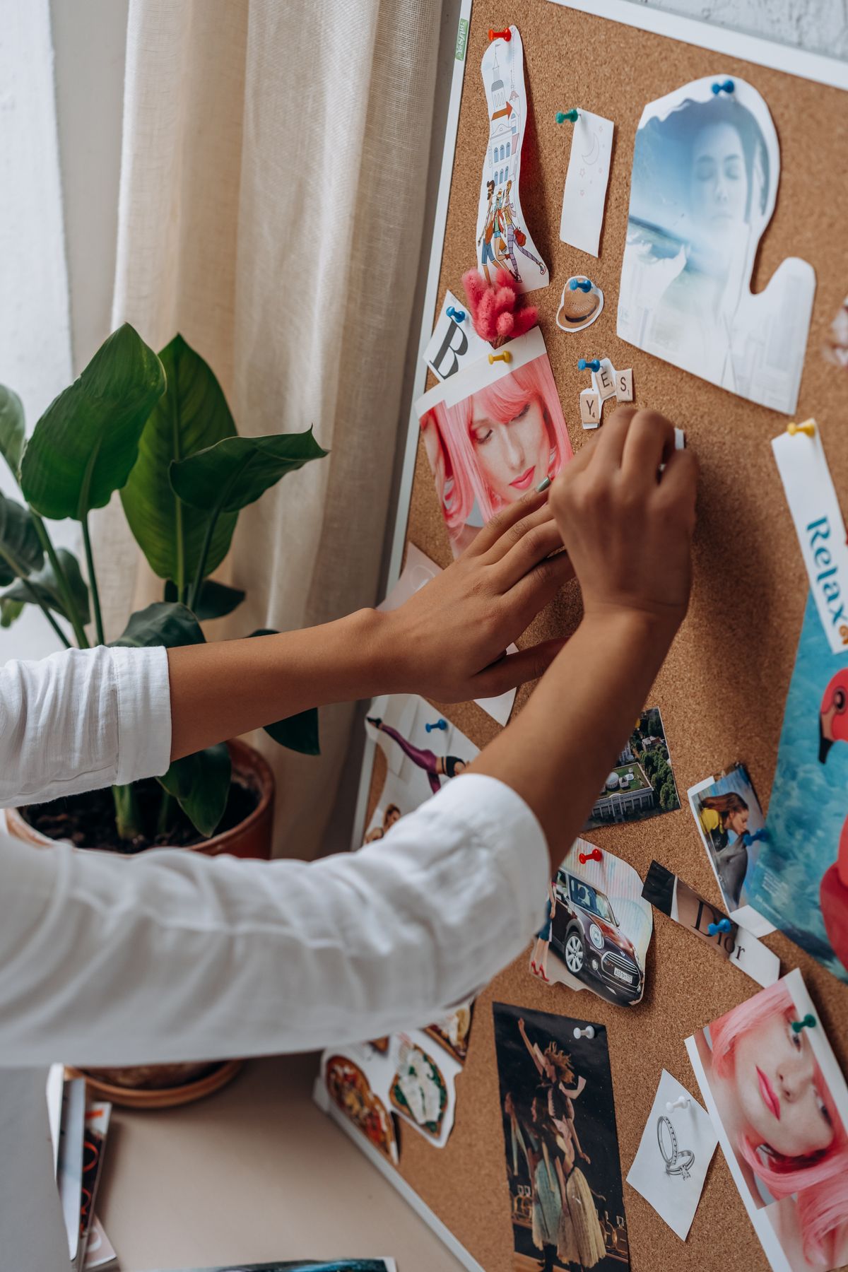 Hands pinning photos to a cork mood board