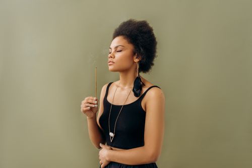 Free Serene young woman practicing aromatherapy with incense stick indoors, promoting wellness. Stock Photo