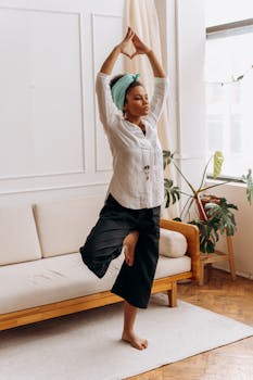 An adult black woman practicing yoga at home in a well-lit room, showcasing healthy living and wellness.