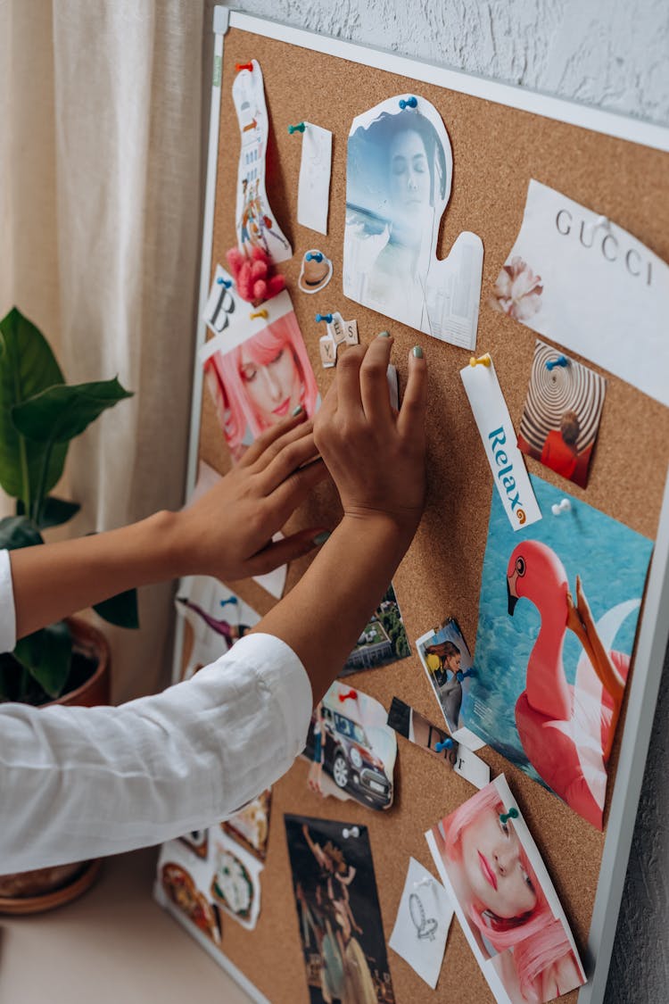 A Hand Sticking Cut Out Magazine On A Cork Board