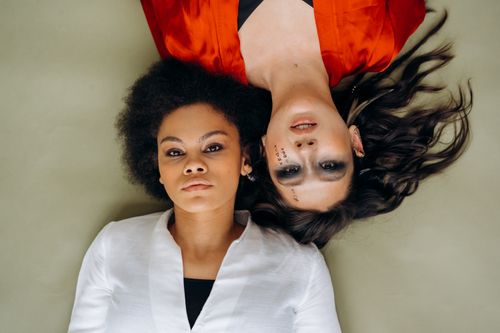Free A creative studio portrait of two women lying down with contrasting expressions and attire. Stock Photo