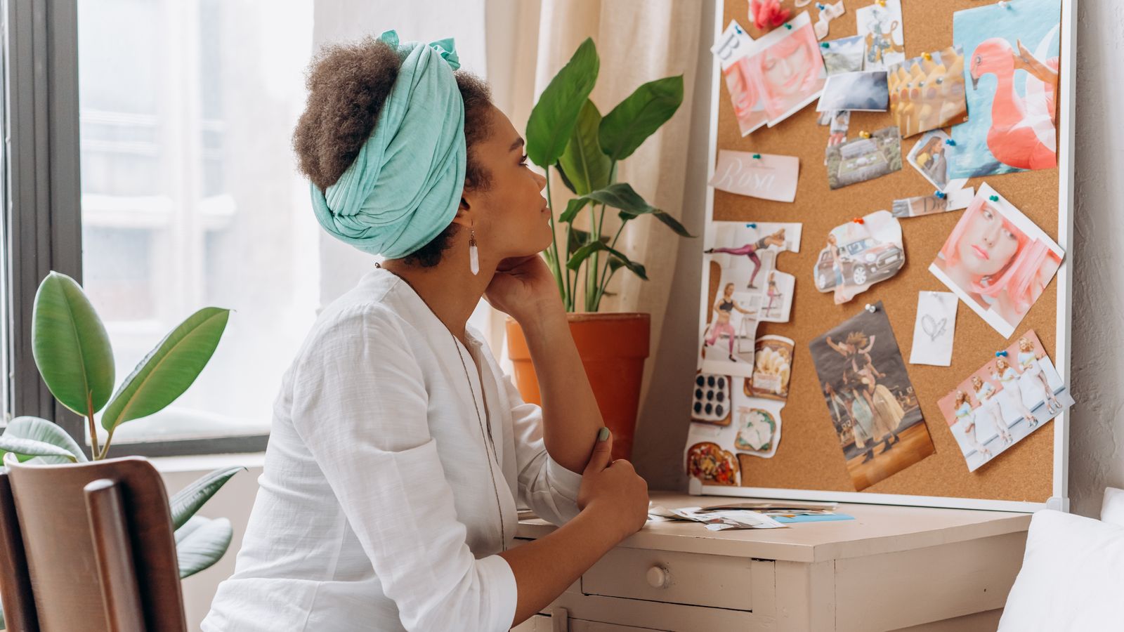 A woman looking at a vision board beside a window with plants