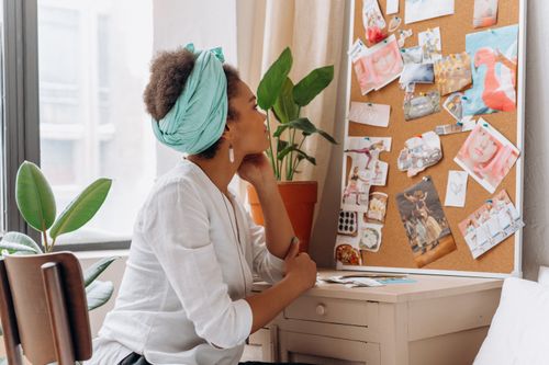 Free African American woman reflecting on a vision board by a window with plants. Stock Photo