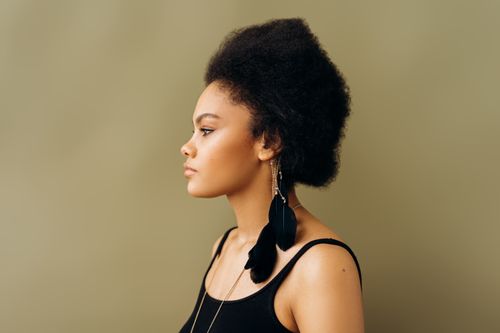 Free Side profile portrait of a woman with natural afro hairstyle and feather earrings against a brown background. Stock Photo