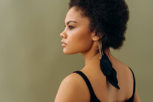 Free A stylish side profile portrait of a woman with distinctive earrings against a neutral background. Stock Photo