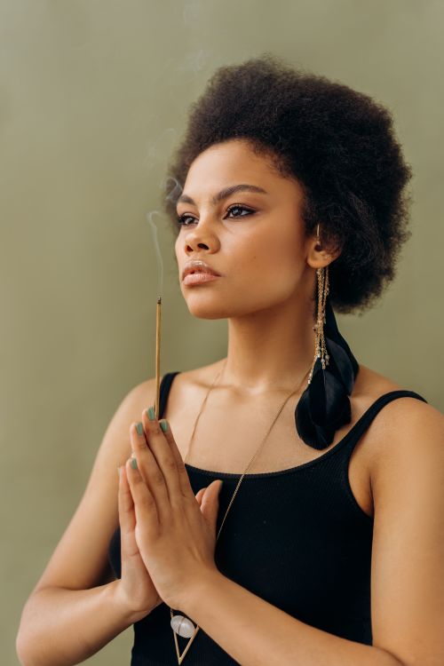 Free Close-up of a woman meditating indoors with a burning incense stick in contemplative posture. Stock Photo