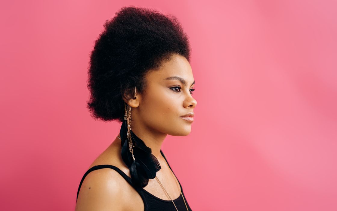 Side profile of a woman with Afro-textured hair against a pink background