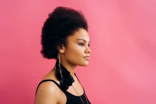 Free A stylish profile portrait of a woman with afro-textured hair against a vibrant pink background. Stock Photo