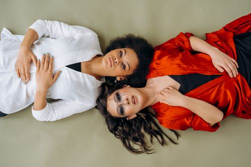 Free Artistic portrait of two women in stylish attire lying on a neutral background. Stock Photo