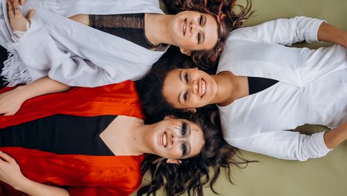 Free Three smiling women lying on the floor wearing vibrant clothing, symbolizing joy and friendship. Stock Photo