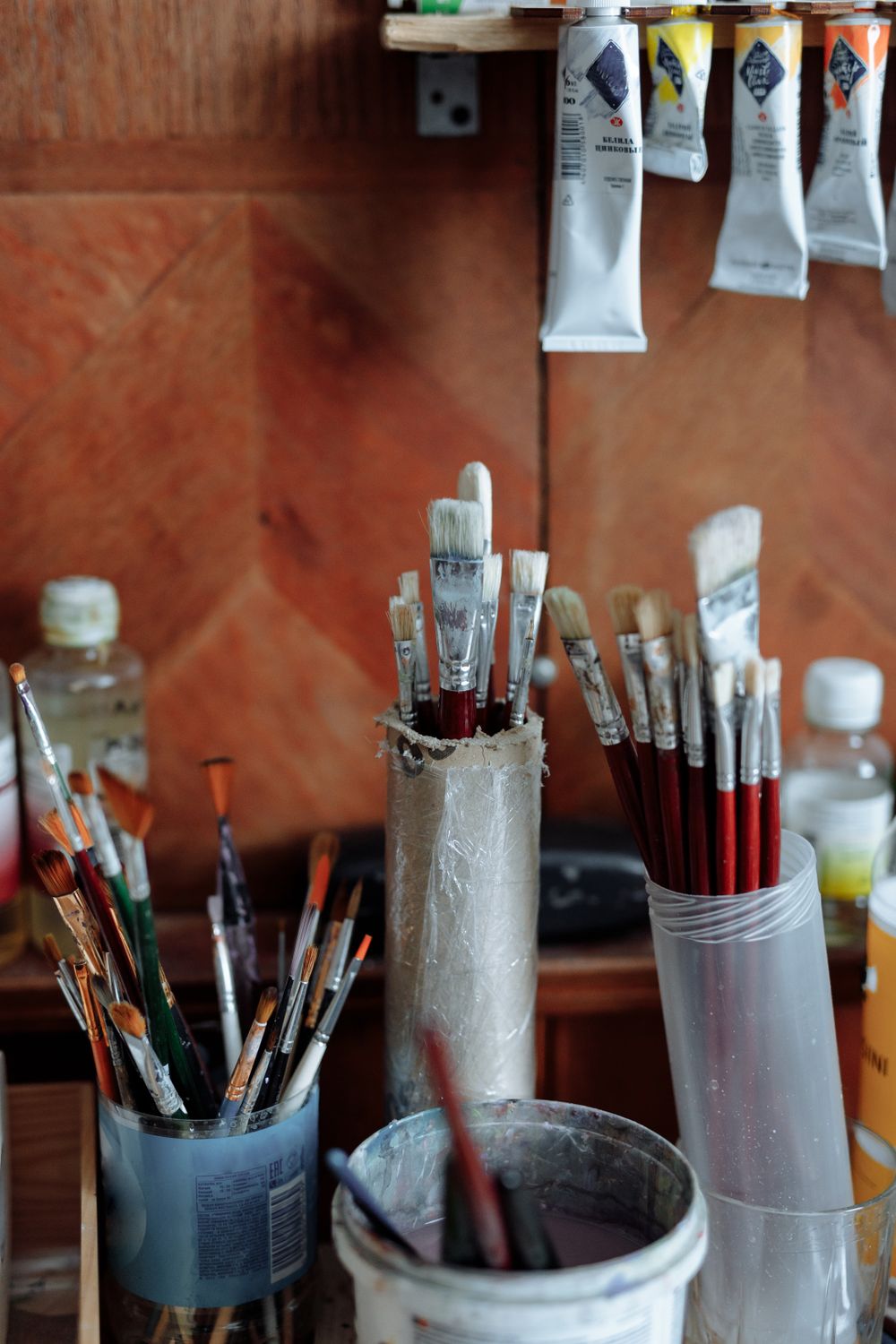 Studio bench with brushes standing in a pot beside paint tubes