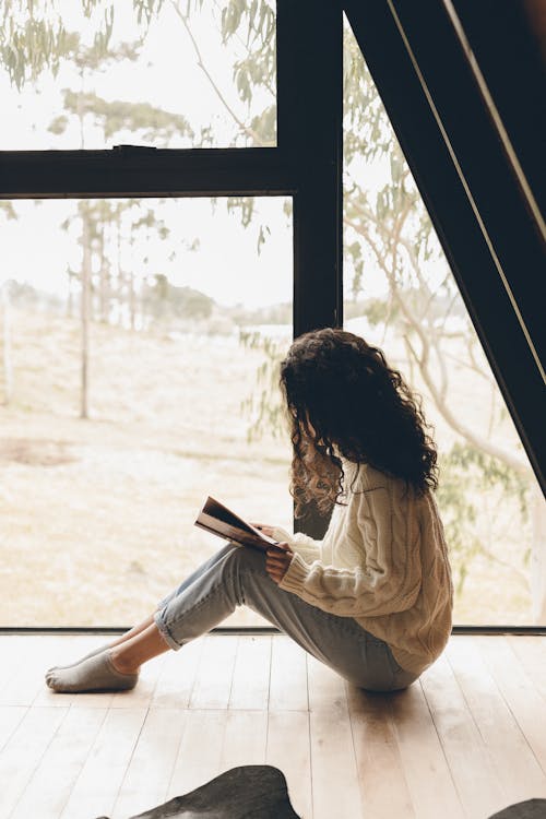 Free Woman Sitting on the Floor While Reading a Book Stock Photo