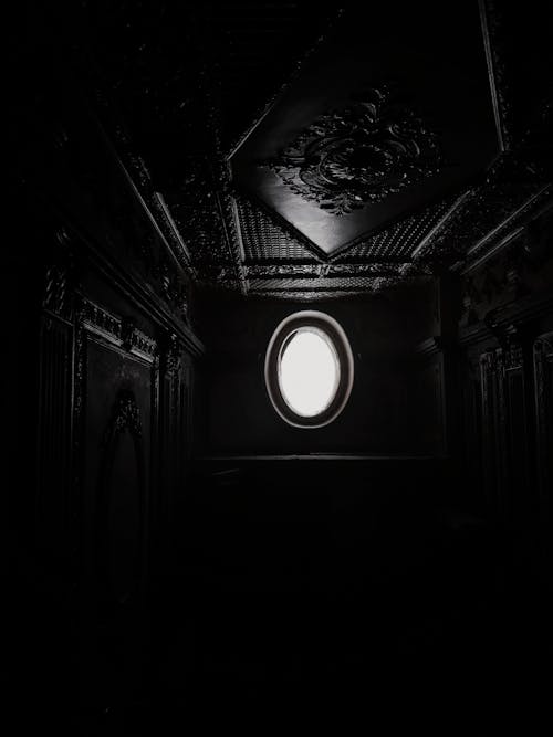 Black and white of long narrow dark corridor with light coming from window and ornamental elements on ceiling and walls