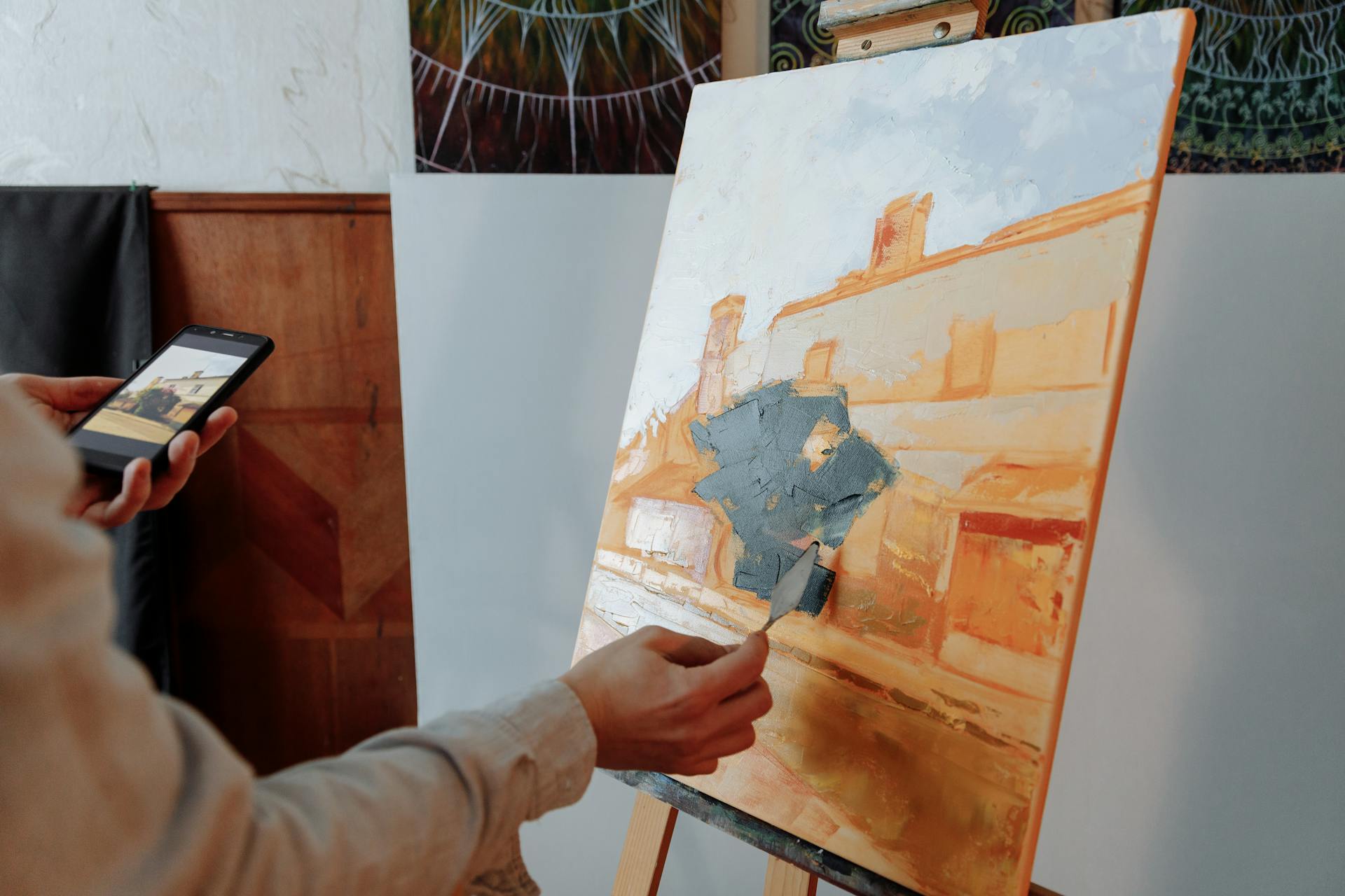 Artist using smartphone reference while painting a canvas indoors.