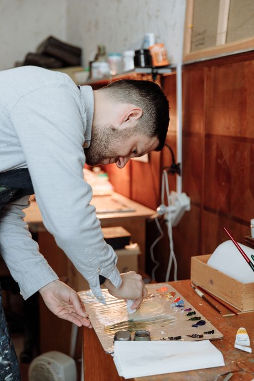 Free Focused male artist blends colors on a palette in his studio. Creating art indoors. Stock Photo