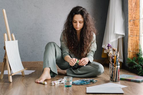 Free A Woman Sitting on the Floor and Opening a Paint Tube Stock Photo