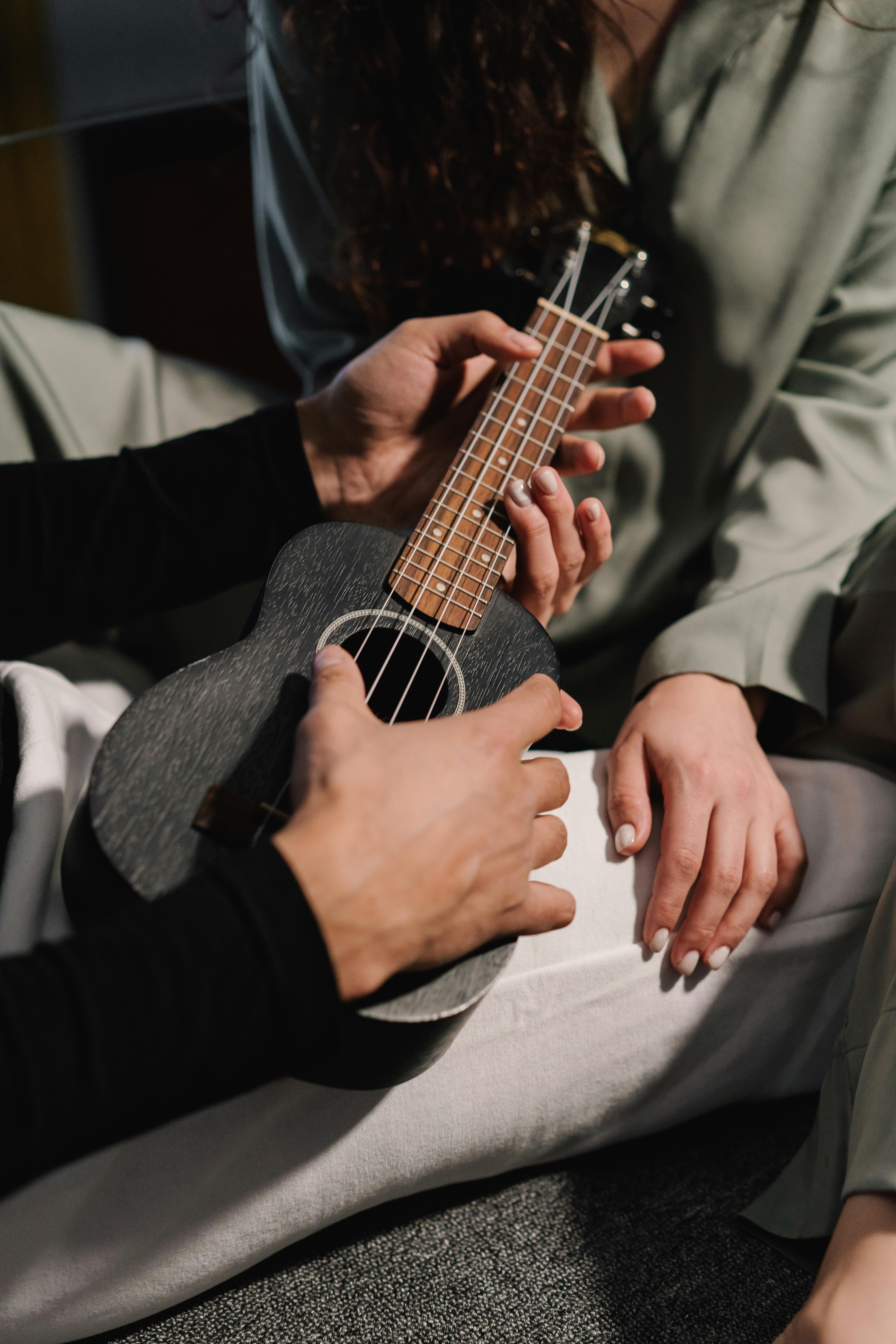 Two adults engaged in playing a ukulele, focusing on hands and the instrument in a cozy setting.