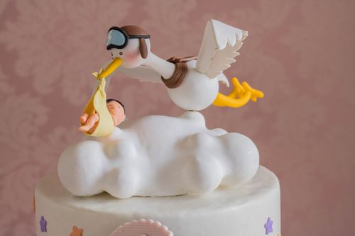 Free Close-up of a whimsical stork carrying a baby figurine on a cake top, ideal for baby showers. Stock Photo