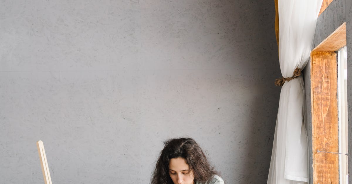 A young woman in casual attire painting on the floor of a modern studio with natural light.