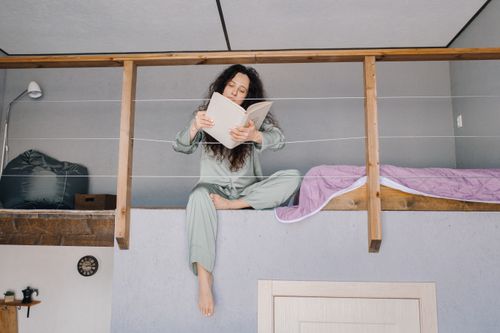 Free Woman in sleepwear reading a book on a loft bed, creating a cozy home vibe. Stock Photo