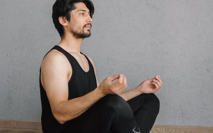 Asian man in activewear meditating in a seated yoga pose indoors for well-being and mindfulness.