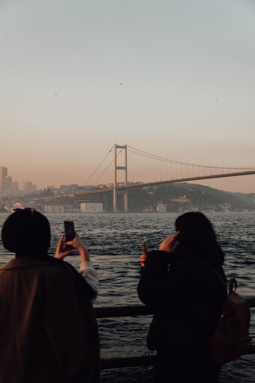 Woman taking photo of bridge over river with friend from embankment