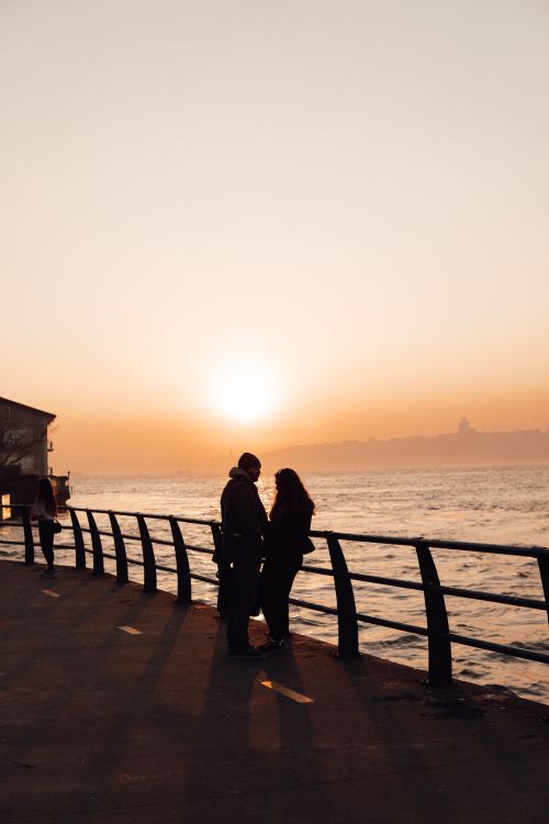 Free Silhouette of couple standing on embankment by fence near river and admiring sunset sky Stock Photo