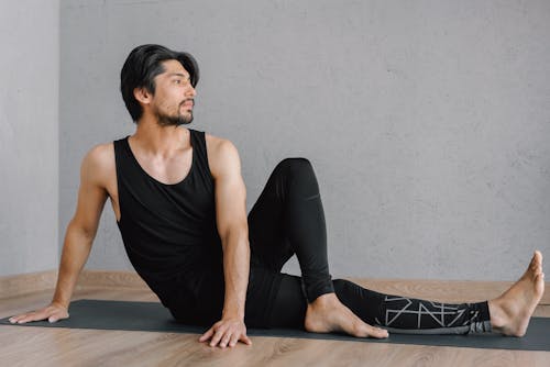 Man in a Black Tank Top Stretching on a Yoga Mat