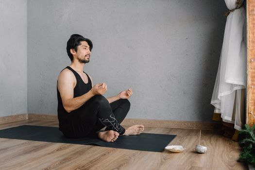 Asian man practicing meditation indoors on a yoga mat, focusing on well-being and mindfulness.