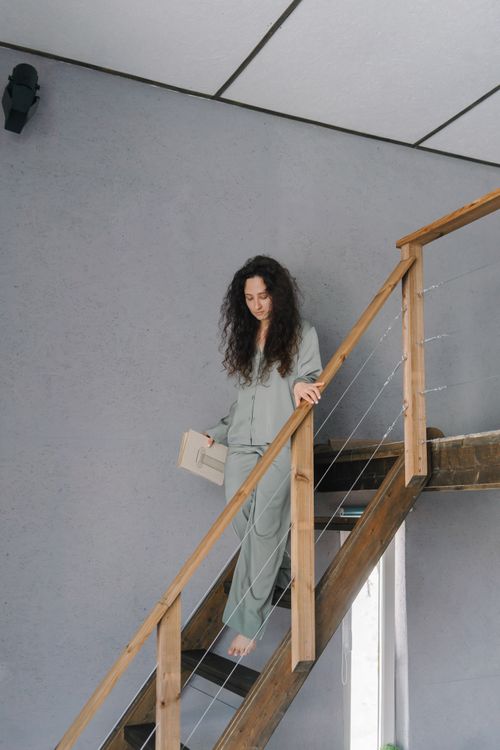 Free Woman with long curly hair descends indoor wooden stairs holding a book. Stock Photo