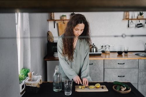 Free A woman prepares a refreshing drink by slicing lemon and ginger in a stylish kitchen. Stock Photo