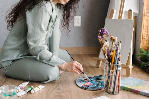 Woman in Gray Sleepwear Sitting On The Floor Holding A Paintbrush