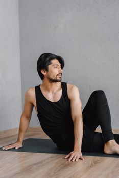 A man in black activewear practicing yoga indoors on a mat, promoting wellness.