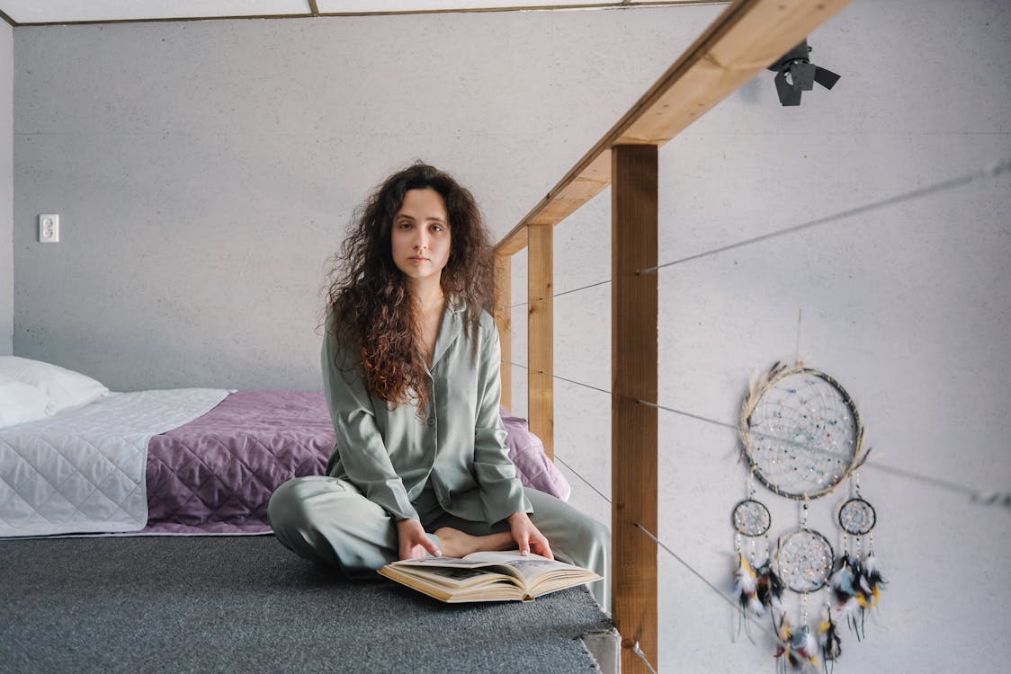 Free A Woman Sitting with a Book Near Her Bed Stock Photo