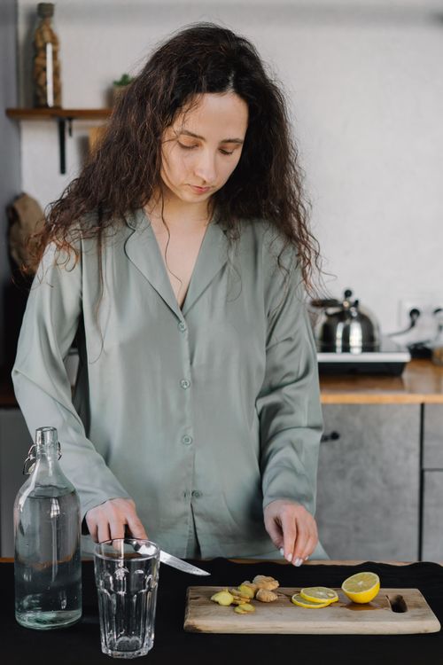 Free A woman slicing ginger and lemon in a kitchen, preparing a herbal drink. Stock Photo