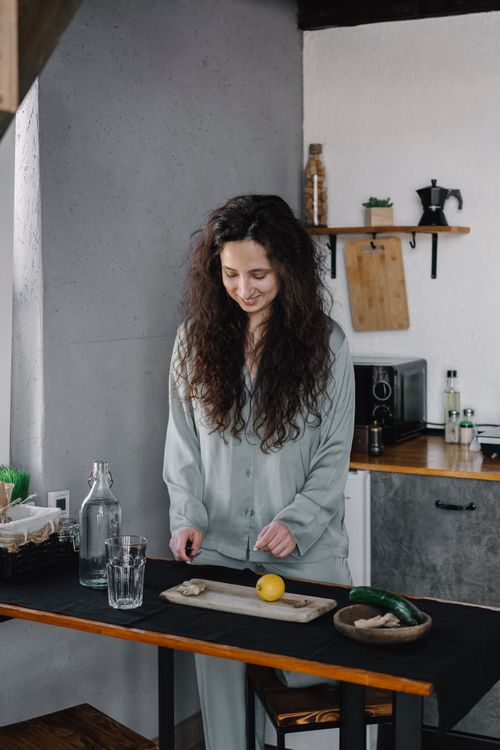 Free A woman in pajamas prepares a drink with lemon and ginger in a stylish kitchen. Stock Photo