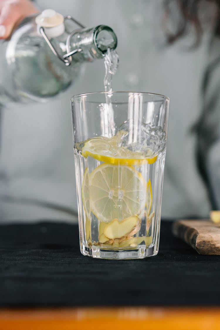 Close-Up Shot Of A Person Pouring Water On A Glass With A Lemon