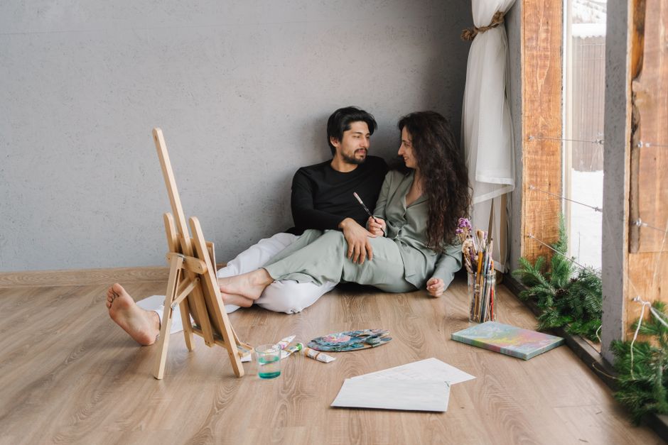 Como a Criatividade Pode Melhorar Seus Relacionamentos Pessoais 2 Happy couple sitting on the floor inside, enjoying a painting session with natural light.