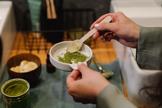 Close-up of hands blending green powder for beauty treatment in a home setting.