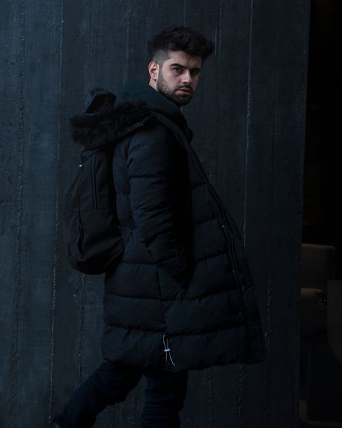 Free Portrait of a man in a black puffer jacket with a backpack in an urban setting. Stock Photo