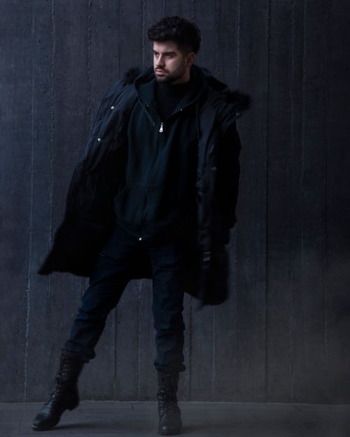 Free Young bearded man in dark winter attire poses against a wooden wall, exuding style and confidence. Stock Photo